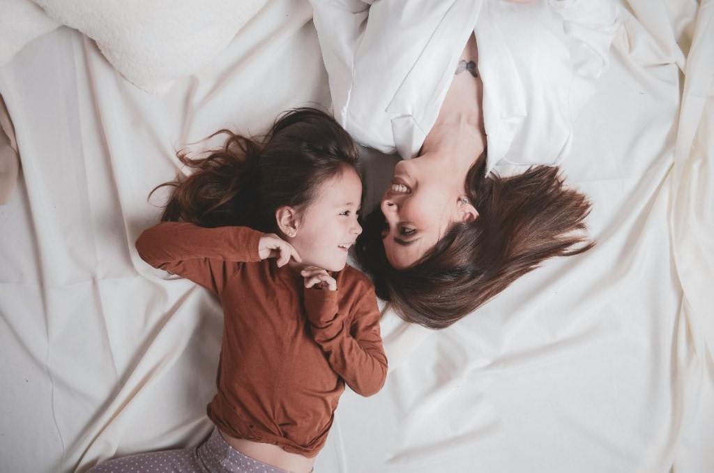 Mother and young daughter lying on a bed and smiling at each other